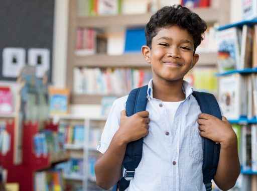 Um estudante sorridente na biblioteca da escola com uma mochila nas costas.